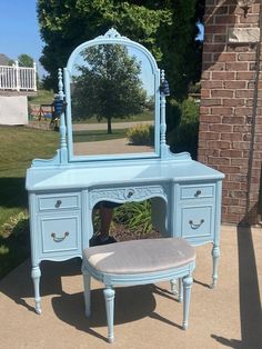 a blue vanity with mirror and stool in front of a brick building on the sidewalk