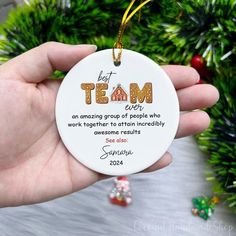 a person holding a christmas ornament with the words team on it in front of a tree