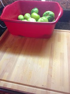 a red bowl filled with green peppers sitting on top of a wooden cutting board next to an oven