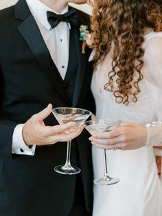 a man in a tuxedo holding a martini glass next to a woman in a white dress