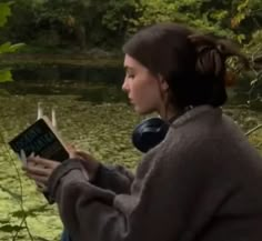 a woman sitting in front of a pond reading a book