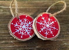 two red ornaments with white snowflakes are hanging from twine on wooden planks