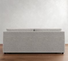 a gray couch sitting on top of a wooden floor next to a white wall in an empty room