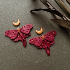 two pink butterfly shaped earrings sitting on top of a table next to leaves and a plant