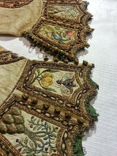 three pieces of cloth with embroidered designs on them sitting on top of a white tablecloth