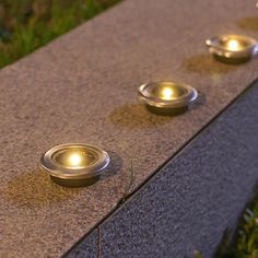 three metal bowls sitting on the side of a cement wall next to grass and flowers