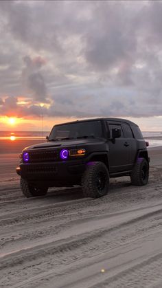 a black truck parked on top of a beach next to the ocean at sunset or dawn