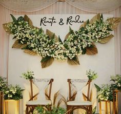 two wooden chairs sitting next to each other in front of a wall with flowers on it