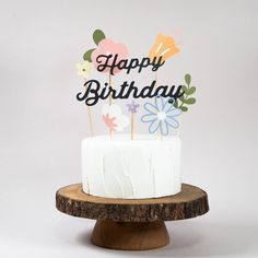 a birthday cake on a wooden stand with flowers and happy birthday sign in the middle