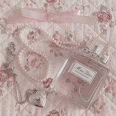 a bottle of perfume sitting on top of a bed next to a heart shaped necklace