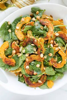 a white bowl filled with spinach and squash salad