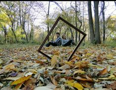 two people sitting on the ground with leaves in front of them and one person taking a selfie