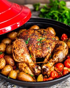 a pan filled with chicken, potatoes and tomatoes on a table next to a red pot