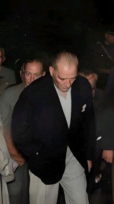 a man in a black jacket and white pants is walking through the crowd with his hand on his hip