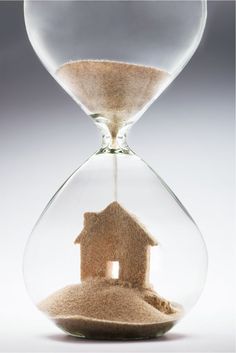 an hourglass with a house in it and sand falling out of the top half