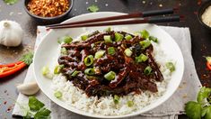 a white plate topped with rice and meat covered in sauce next to chopsticks