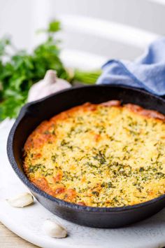 a casserole dish with cheese and herbs in it on a white plate next to garlic