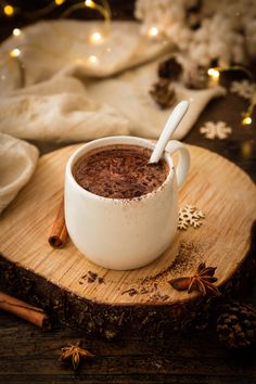 a cup of hot chocolate is sitting on a wooden board with cinnamons and christmas lights in the background