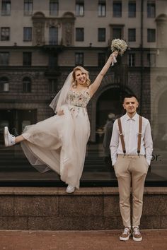 a bride and groom posing for a photo in front of a building with their hands in the air