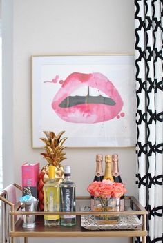 a bar cart filled with bottles of champagne, pineapples and pink lipstick prints