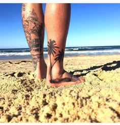 a person standing on top of a sandy beach next to the ocean with tattoos on their legs