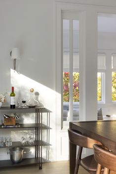 a dining room table and some chairs in front of a book shelf with wine bottles on it