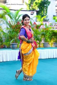 a woman in an orange and blue sari is dancing on a stage with palm trees behind her