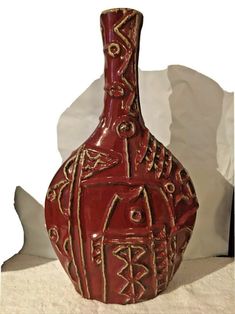 a red vase sitting on top of a table next to a white sheet covered wall