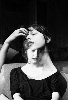 a black and white photo of a woman with her hands on her head, looking at the camera