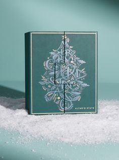 a green christmas card sitting on top of snow covered ground next to a blue wall