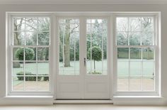 an empty room with two double doors and windows on either side of the door, looking out onto a yard