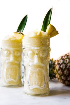 two glasses filled with pineapple juice sitting on top of a counter next to a pineapple