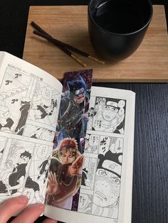 an open comic book sitting on top of a table next to a cup of coffee