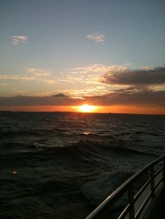 the sun is setting over the ocean as seen from a boat on the water's edge