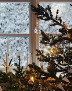 a small christmas tree in front of a window with candles and ornaments on the windowsill