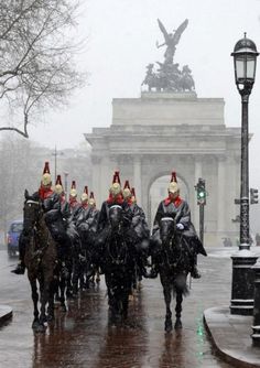 a group of men riding on the backs of horses down a rain soaked street in front of a monument