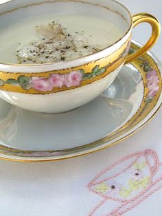 a cup and saucer sitting on top of a white tablecloth with pink flowers