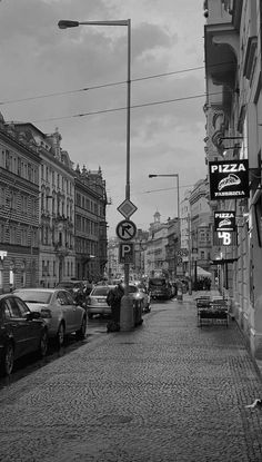 black and white photograph of cars parked on the side of a street next to tall buildings