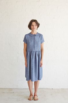 a woman standing in front of a white wall wearing a blue dress and brown sandals