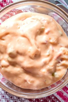 a glass bowl filled with sauce on top of a red and white table cloth next to a fork