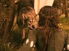 a woman standing next to a wolf on top of a lush green field