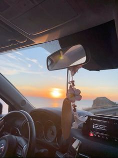 the sun is setting over the ocean as seen from inside a car with steering wheel and dashboard