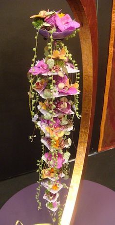 a tall vase with flowers on it sitting on a purple tablecloth covered table top