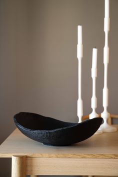 a black bowl sitting on top of a wooden table with candles in the back ground