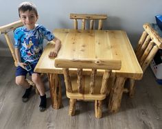 a young boy sitting at a wooden table with chairs around him and smiling for the camera