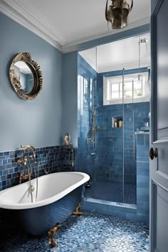 a bathroom with blue tiles and a claw foot bathtub in the corner, along with a round mirror on the wall