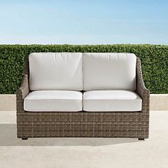 a white couch sitting on top of a cement floor next to a green hedge covered wall