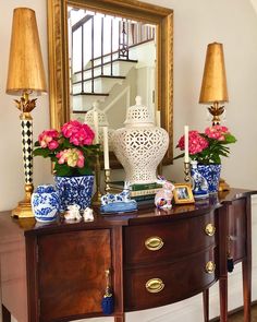 a table with vases and flowers on it in front of a mirror