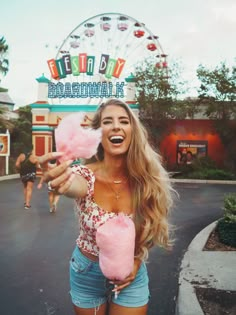 a woman holding a pink lollipop in front of a ferris wheel at disneyland