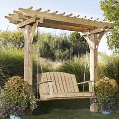 a wooden swing chair sitting on top of a lush green field next to flowers and trees